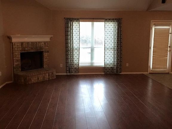 Large vaulted open living area with dark hardwood flooring and fireplace. View of patio and pool from large picture window.