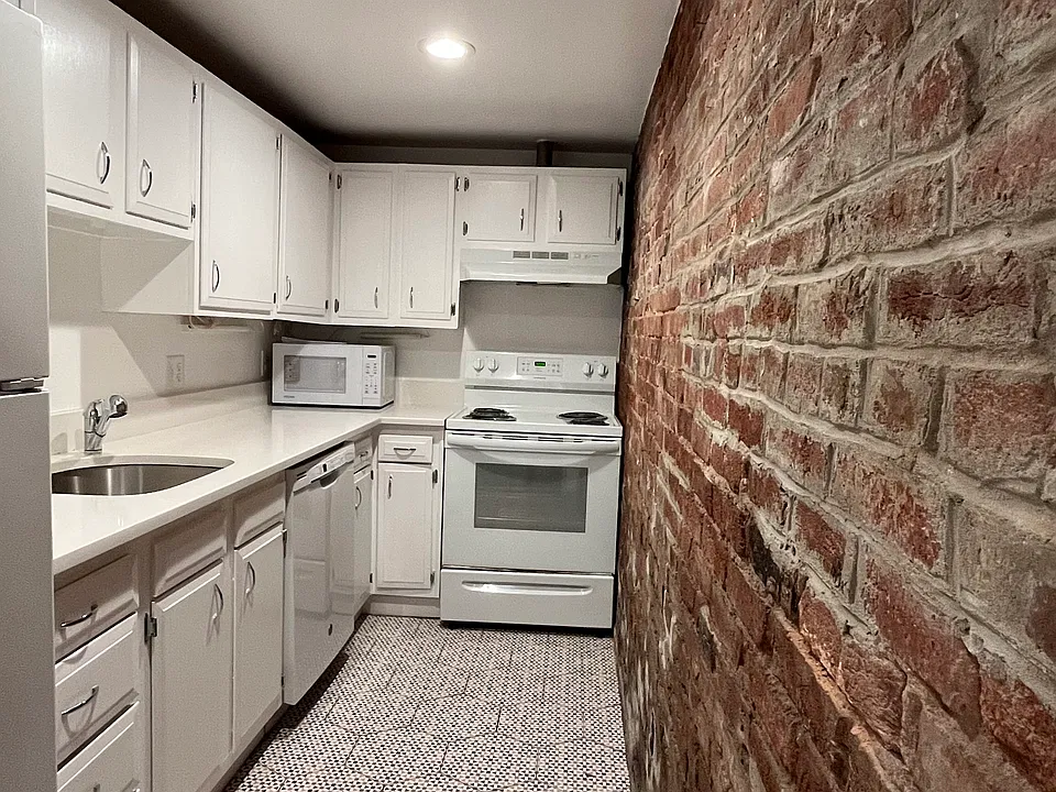 Full kitchen with dishwasher and exposed brick wall