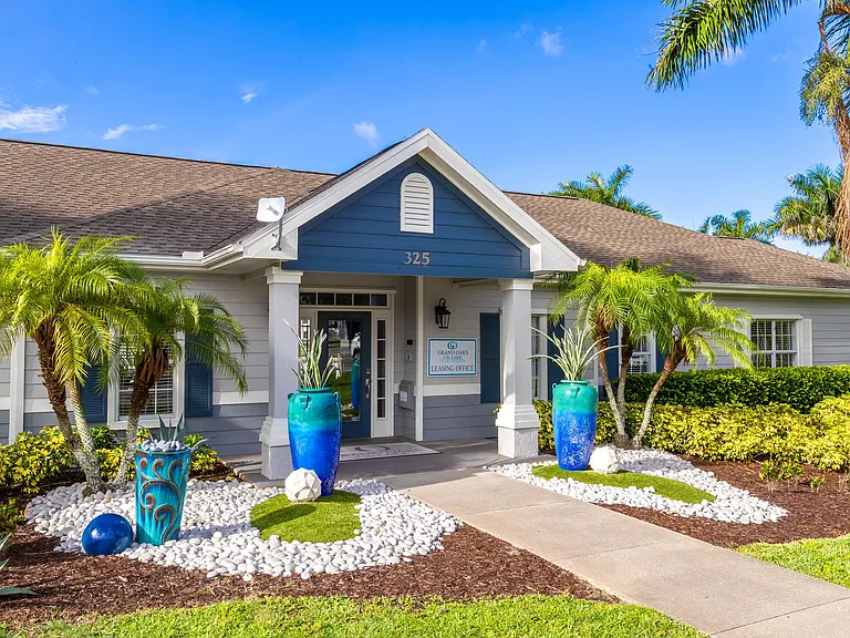 Visit our inviting leasing office surrounded by lush landscaping and tropical palm trees, showcasing the charm of Grand Oaks at the Lake Apartments.
