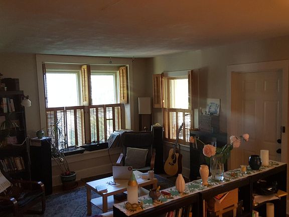 Living room with 10' ceilings, box bay window, hardwood floors, interior wooden shutters. Door leads to enclosed front porch.