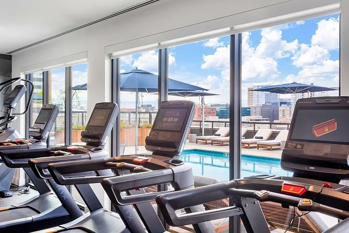 Modern gym with top-of-the-line treadmills and panoramic views of the city skyline and outdoor pool area.
