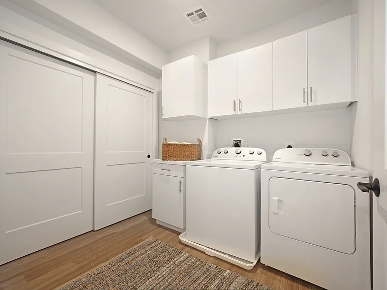 Modern in-unit laundry room with sleek white cabinetry, efficient full-sized washer and dryer, and elegant sliding doors.