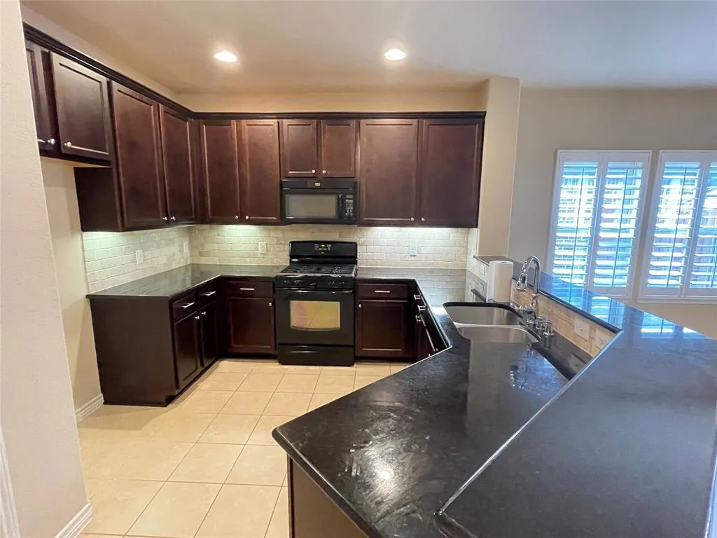 Kitchen featuring dark brown cabinets, kitchen peninsula, backsplash, black appliances, and sink - 12101 Walden Wood Dr