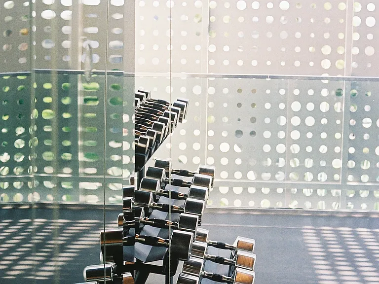 State-of-the-Art Fitness Studio with Architectural Detailing & Outdoor Yoga Terrace _ This exclusive fitness space features a sleek, contemporary design with custom perforated metal panels that filter in natural light while maintaining privacy.