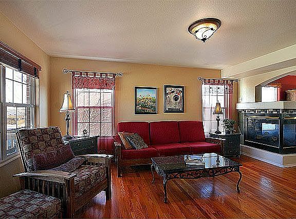 Bright living room features oak floors, dual-sided pedestal gas log fireplace,