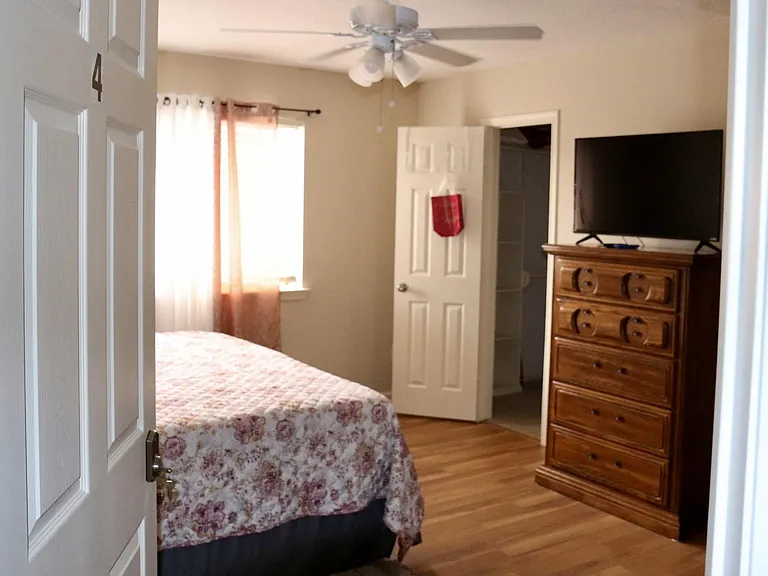 Private bedroom with wood-style flooring, ceiling fan, and a closet, plus a dresser and TV for convenient storage.