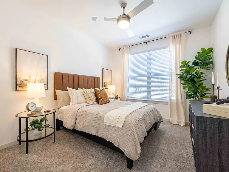 The secondary bedroom in this Garrett Parker B1 floor plan includes a queen size bed, wall to wall carpet, and a large window.