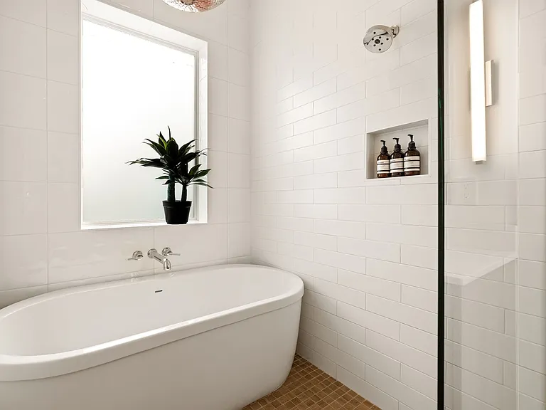Modern bathroom featuring a freestanding soaking tub with wall-mounted chrome fixtures, a large frosted window, and white subway tile walls