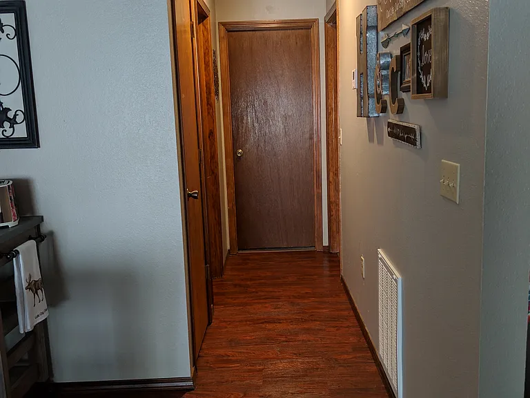 Standing at edge of kitchen looking down hall. First door on left is coat closet, next is door to bathroom, at the end of hall is a bedroom and door on right is the master suite