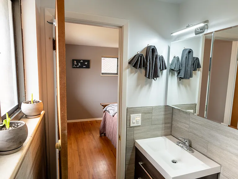 View from the primary bathroom to the primary bedroom, showing the west-facing window of the bathroom and the north-facing window of the bedroom plus the medicine cabinet and the vanity.