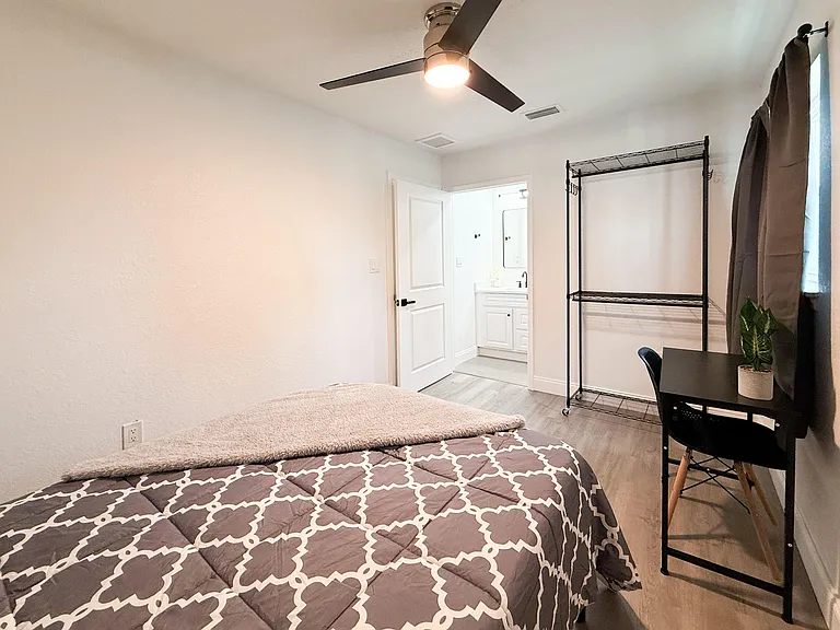 Furnished bedroom with ceiling fan, window treatments, desk area, and open shelving for added storage.