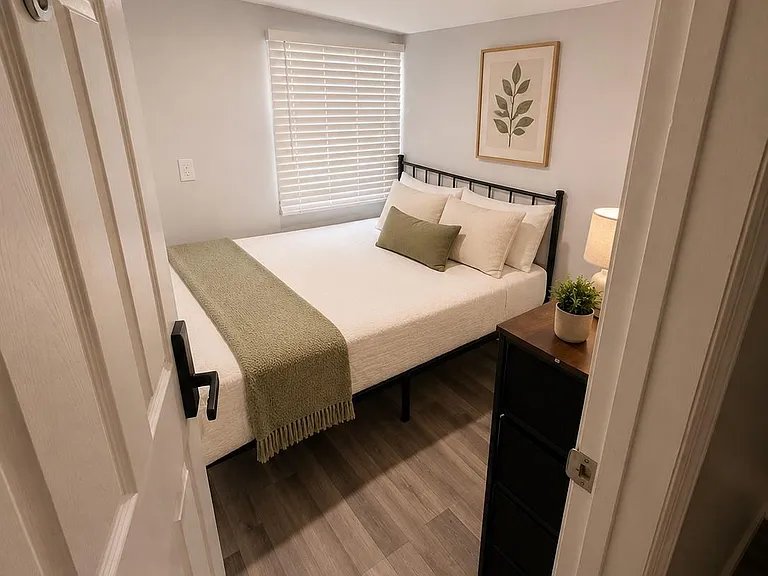Efficient bedroom with a full-size bed, bedside lighting, and a window with blinds for privacy and light control.