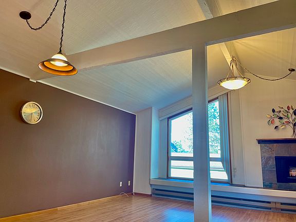 Open living room and dining room with wooden decorative beams and hanging chandeliers.