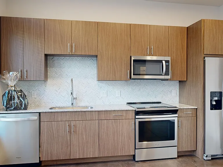 Apartment kitchen with stainless steel appliances, granite countertops, and polished concrete flooring.