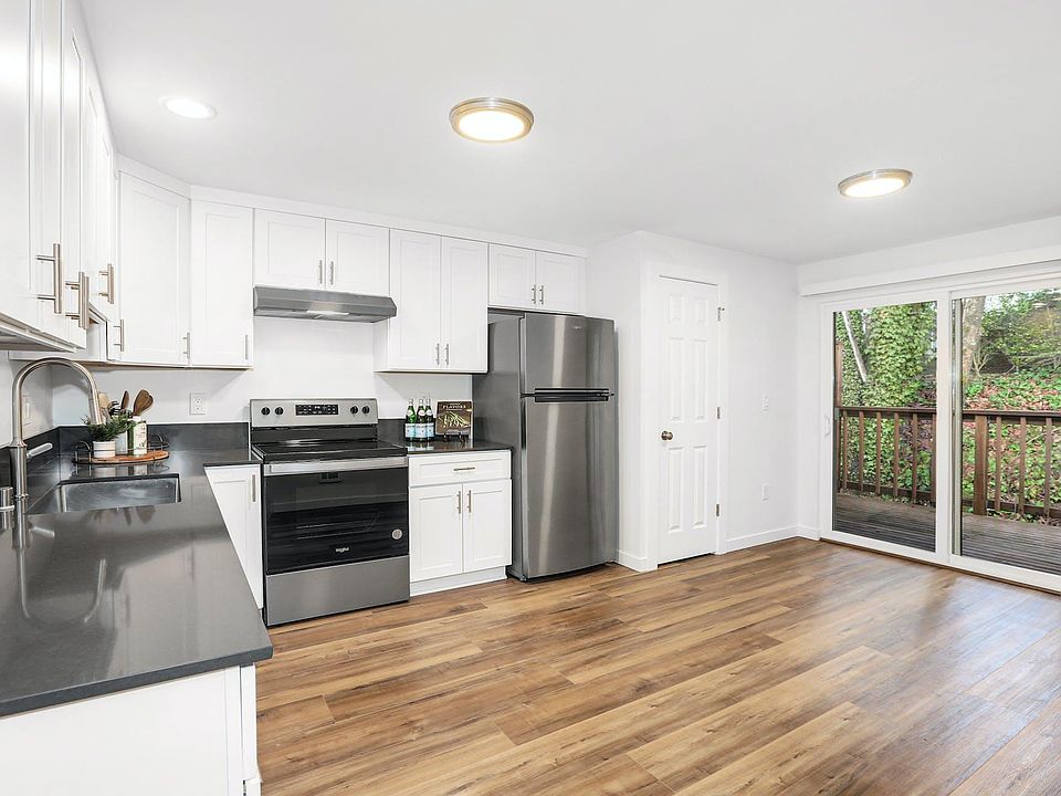 Kitchen looks out to newer private cedar deck with storage locker for additional storage options. View of trees and greenery.