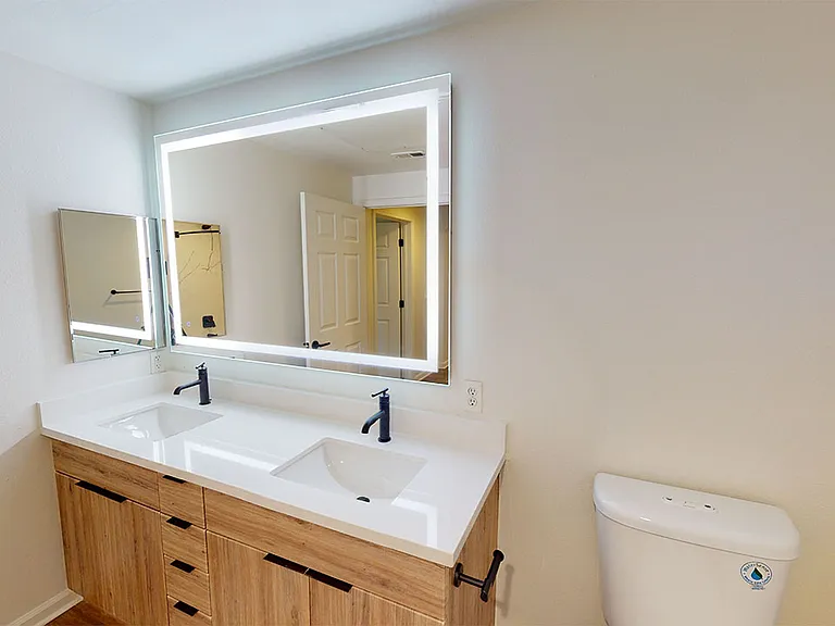 Apartment Bathroom with wood-style flooring, double sinks and LED vanity mirror.