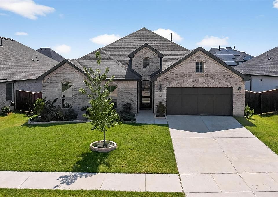 French country style house with brick siding, driveway, a garage, a front lawn, and a shingled roof