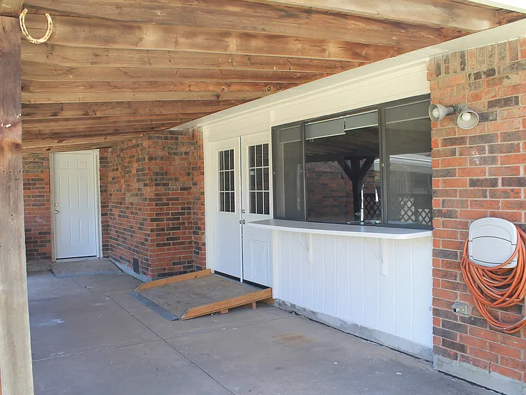 A double door leads to a covered patio with a convenient outdoor bar area. A ramp provides easy accessibility. The garage door is accessible from the patio