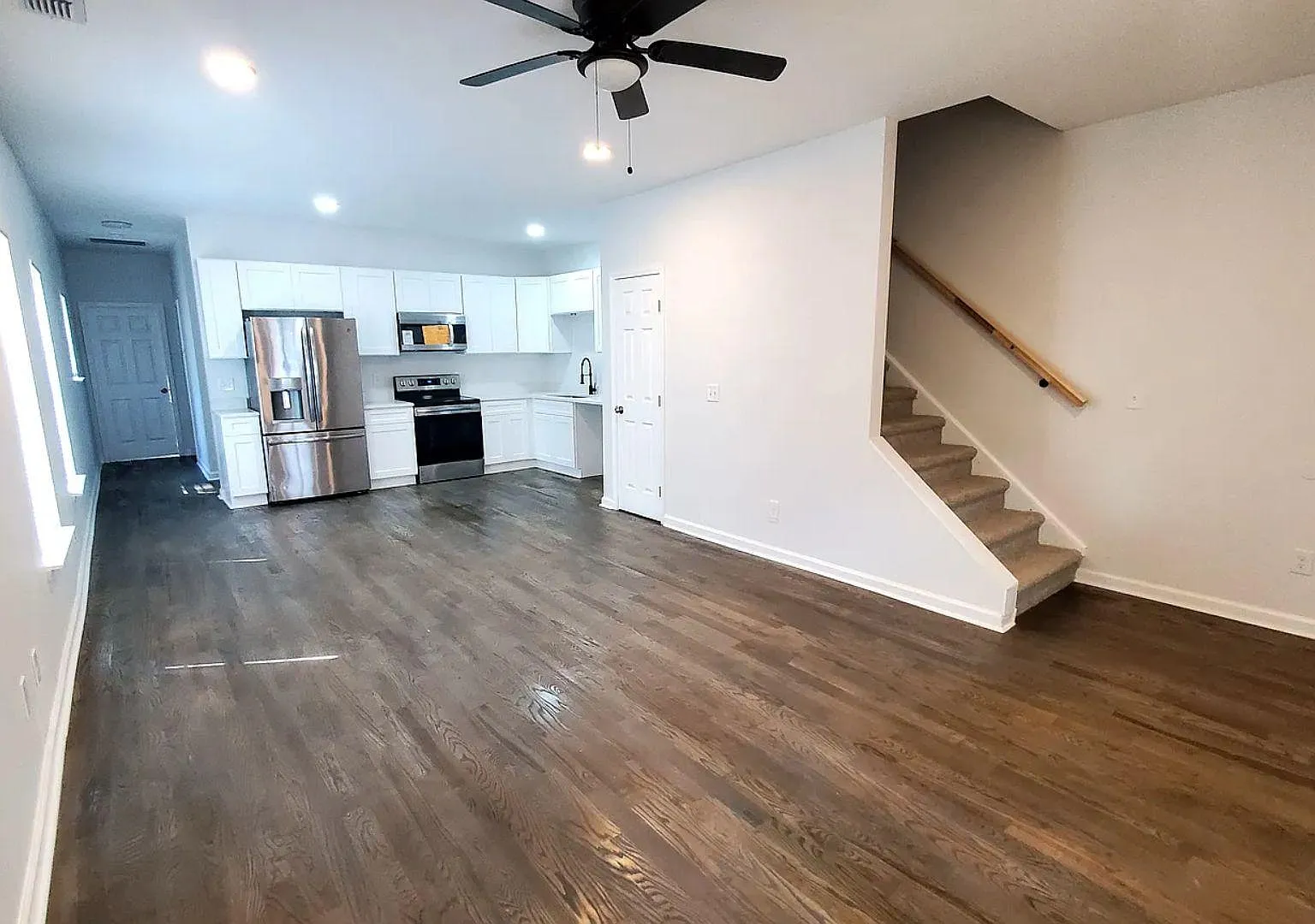 Open-concept living area with durable wood-look flooring, ceiling fan, and a connected kitchen with stainless appliances.