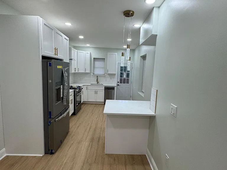 Galley kitchen with white cabinetry, quartz-look counters, stainless appliances, and peninsula seating under pendant lights.