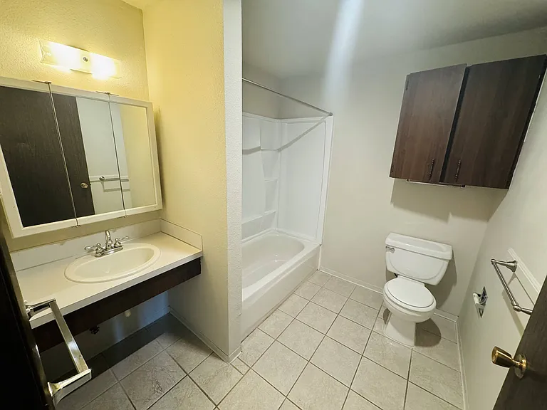 This spacious bathroom features a full tub and shower, ample storage, and easy-care tile flooring for everyday comfort.