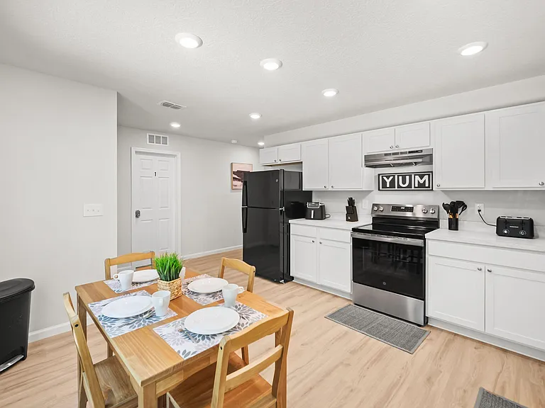 Open kitchen with ample white cabinetry, full-size range and refrigerator, and an adjacent dining area for easy meals.