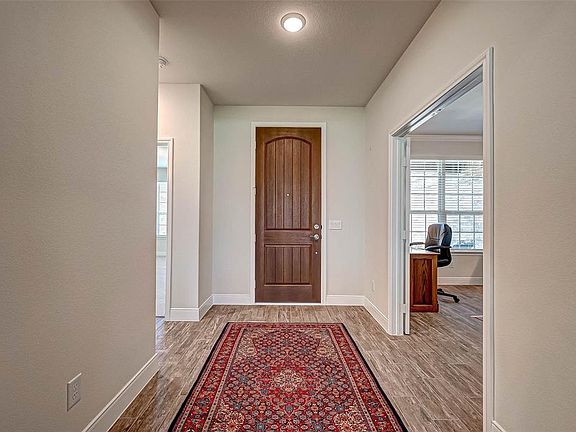 The spacious entrance foyer features wood-like tile flooring that continues throughout the whole of the home. Notice the handsome two panel arched rich wood front door. The opening to the right leads to your own private home study with double glass p