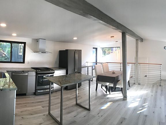 Sunny & open floor plan Living room, dining area, new custom gourmet kitchen with gas stove, quartz countertops, matte stainless steel appliances. Grey wood tone laminate flooring & white walls throughout home.