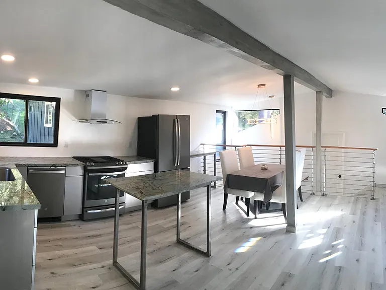 Sunny & open floor plan Living room, dining area, new custom gourmet kitchen with gas stove, quartz countertops, matte stainless steel appliances. Grey wood tone laminate flooring & white walls throughout home.