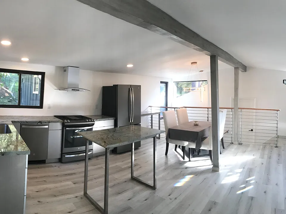 Sunny & open floor plan Living room, dining area, new custom gourmet kitchen with gas stove, quartz countertops, matte stainless steel appliances. Grey wood tone laminate flooring & white walls throughout home.
