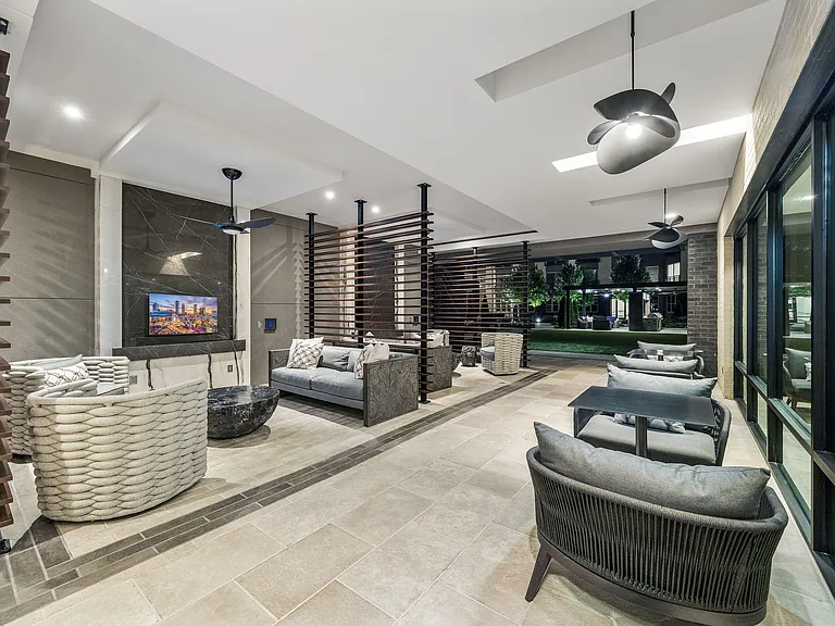 Luxurious open-air lounge area featuring modern seating, stylish ceiling fans, and a beautiful view of landscaped gardens.