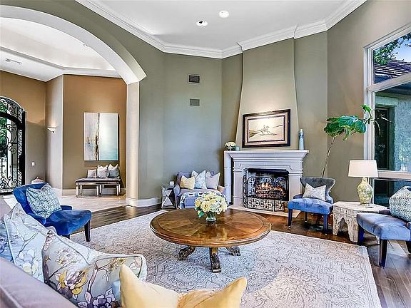 Formal living room with fireplace, piano and floor to ceiling windows with tree views.