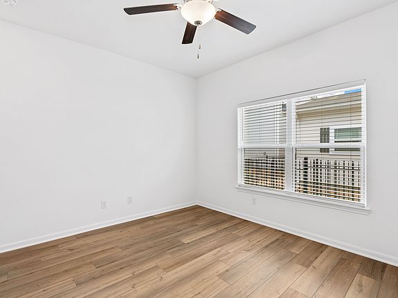 Spacious family room with wood-style flooring, large windows, and a ceiling fan.