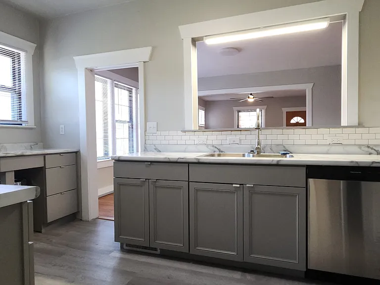 View of the kitchen from the pantry, showing pass-throuth to the formal dining room and custom cabinetry below windows with a space for your trash can. Notice the brand new fixtures and dishwasher!
