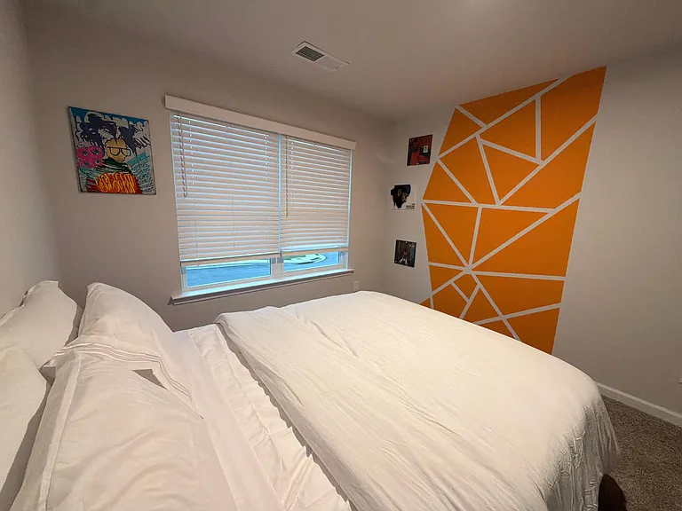 Comfortable bedroom with a full-size bed, window with blinds, and a statement accent wall for a welcoming retreat.