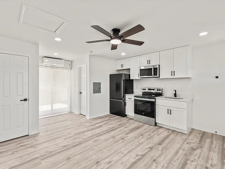 Open-concept living space featuring wood-finish flooring, a contemporary kitchen, white cabinetry, a black refrigerator, and stainless steel appliances