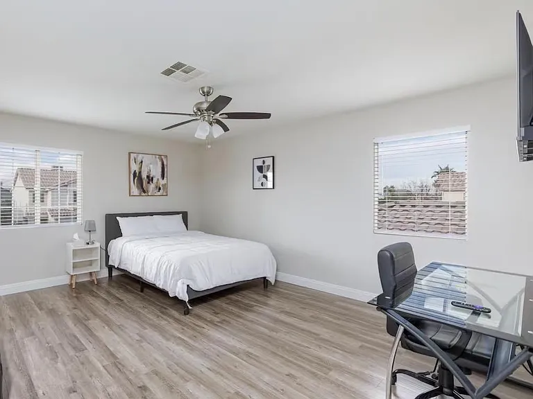 Spacious bedroom with wood-style flooring, ceiling fan, and two windows, plus a dedicated desk/work area.