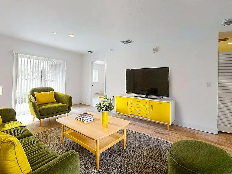 Bright and inviting living room with stylish green and yellow furnishings, featuring a cozy seating area, large TV, and modern decor.