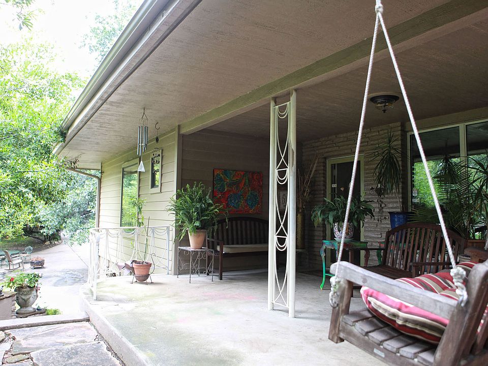 The large front porch faces a pond and is surrounded by trees.