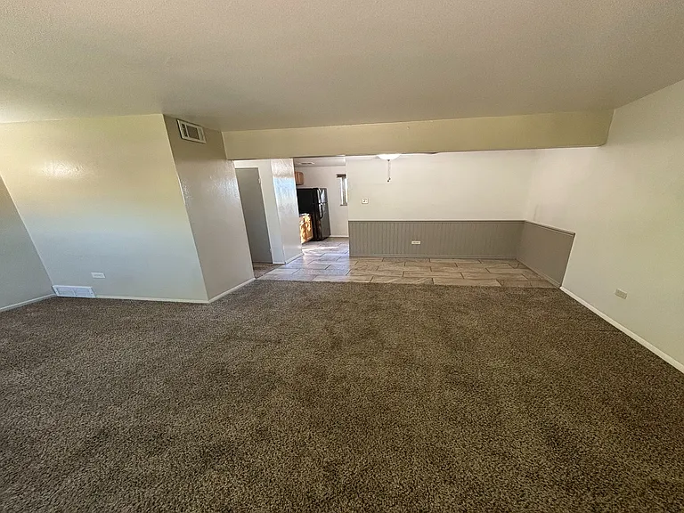 Inviting living area with plush carpet, leading to a cozy dining space and modern kitchen.