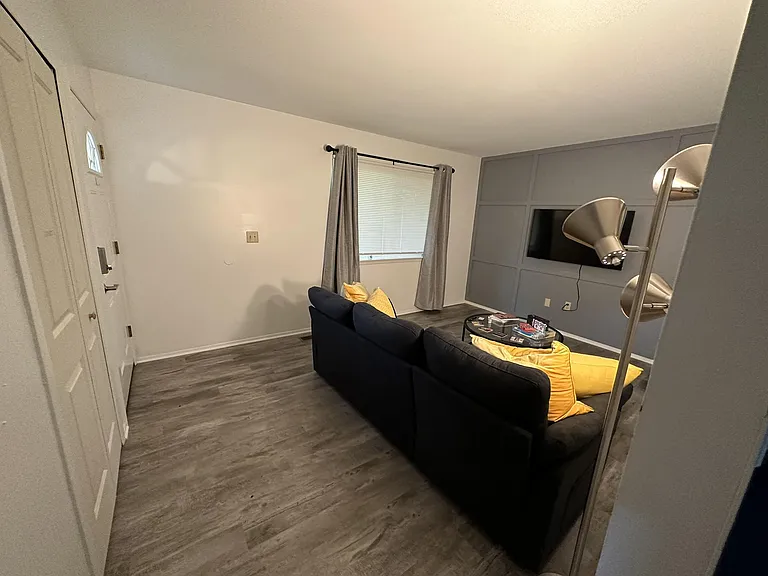 Living room with durable flooring, a seating area, and a wall-mounted TV, plus a window with curtains for natural light.