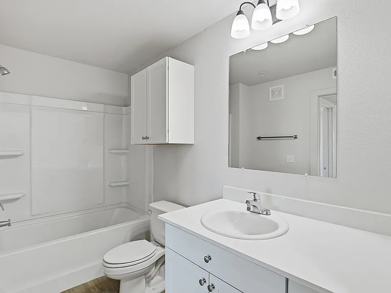 Pristine modern bathroom featuring sleek white cabinetry, elegant fixtures, and a spacious mirror, perfect for a contemporary living space.