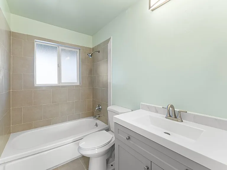 Newly renovated guest bathroom featuring updated shower tile, tile flooring, sleek vanity with modern fixtures and storage. (Mirror not shown in photo.)