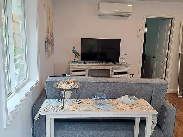 Enter into living room with recessed lighting. Entry Table, Laminate Flooring, Mini Blinds, Heating/Air Conditioning Unit. WiFi and Sofa which folds out into a second bed