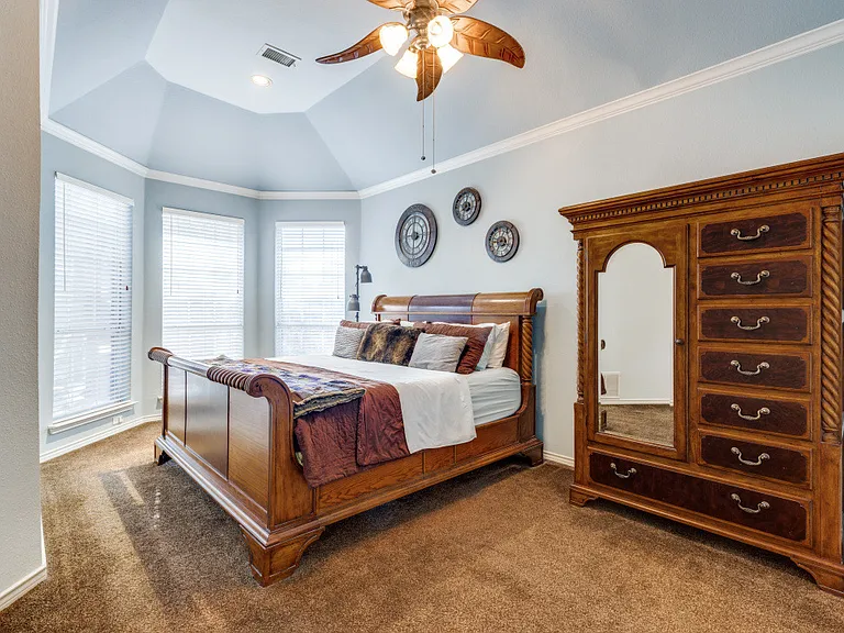 Primary bedroom featuring dark carpet, ornamental molding, a raised ceiling, vaulted ceiling and ceiling fan.