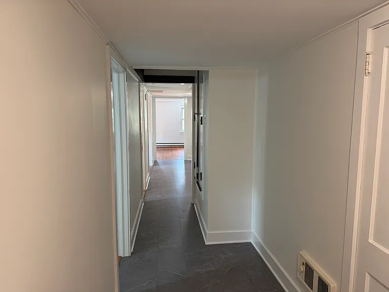 Hallway from primary/laundry area looking towards second bedroom (door on the left), kitchen, and living room.