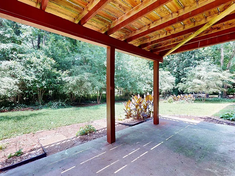 Covered backyard patio with a concrete slab, ideal for outdoor seating, plus a spacious grassy yard with mature trees.