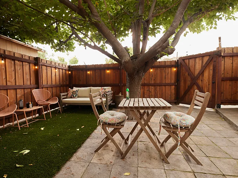 Private yard with synthetic grass, a huge tree that provides great shade, and string lights on a timer.