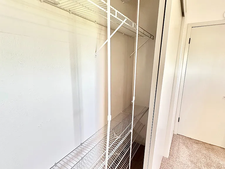 Spacious walk-in closet featuring sleek white wire shelving, perfect for organized storage in a modern apartment.