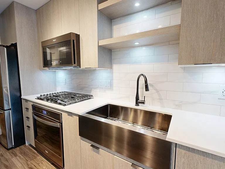 Apartment Kitchen with Stainless Steel Appliances, White Quartz Countertops and wood flooring.